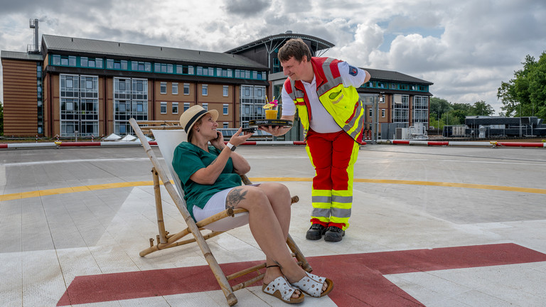 Perspektivwechsel: Notarzt serviert Hauswirtschaftsbereichsleitung Cocktail auf Hubschrauberlandeplatz