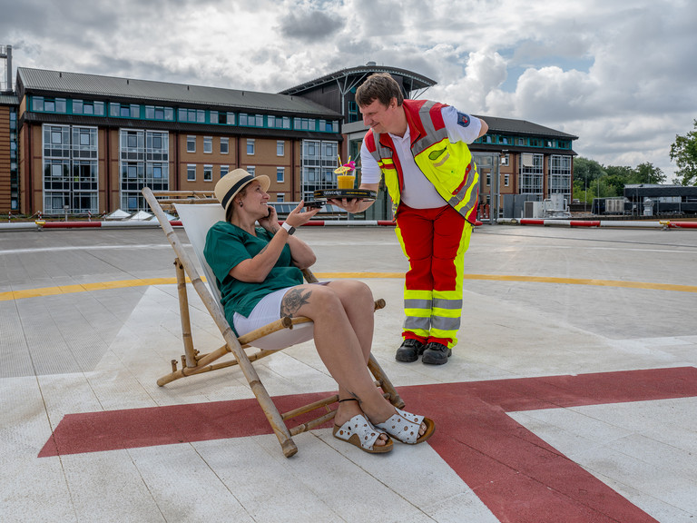 Perspektivwechsel: Notarzt serviert Hauswirtschaftsbereichsleitung Cocktail auf Hubschrauberlandeplatz
