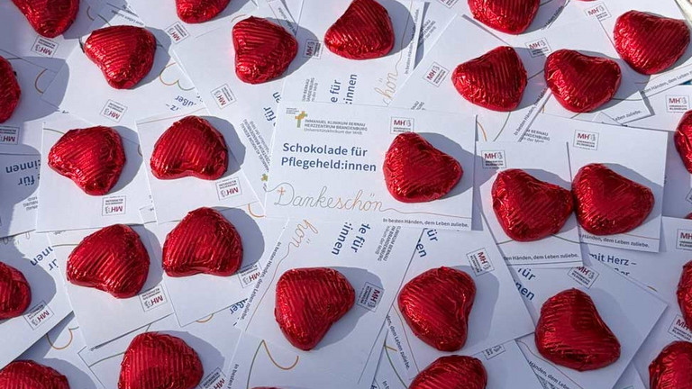 Zahlreiche rot verpackte Schokoherzen liegen um Dankeskarten mit der Aufschrift "Schokolade für Pflegeheld:innen" am Internationalen Tag der Pflegenden im Immanuel Klinikum Bernau Herzzentrum Brandenburg.