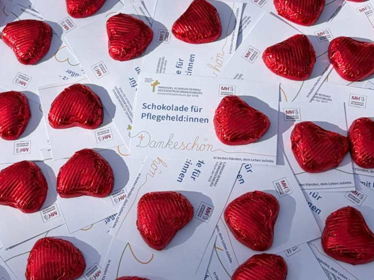 Zahlreiche rot verpackte Schokoherzen liegen um Dankeskarten mit der Aufschrift "Schokolade für Pflegeheld:innen" am Internationalen Tag der Pflegenden im Immanuel Klinikum Bernau Herzzentrum Brandenburg.