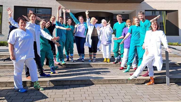 Mitarbeitende des Immanuel Klinikum Bernau stehen vor dem Eingang und zeigen ihre bunten Socken anlässlich des Welt-Down-Syndrom Tages