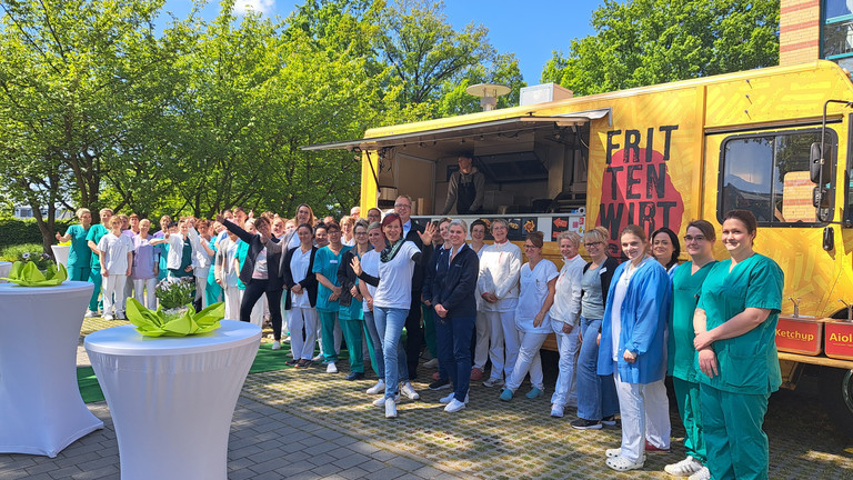 Eine große Gruppe von Pflegefachkräften steht vor einem Food Truck beim Immanuel Klinikum Bernau Herzzentrum Brandenburg und blickt in die Kamera, Tag der Pflegenden, Pflegekräfte Brandenburg, Florence Nightingale Eine große Gruppe von Pflegefachkräften steht vor einem Food Truck beim Immanuel Klinikum Bernau Herzzentrum Brandenburg und blickt in die Kamera beim Tag der Pflegenden