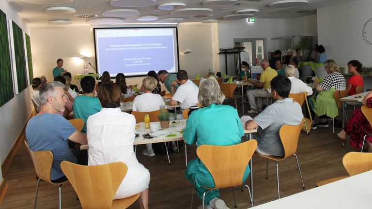 Teilnehmende Hausärztinnen und Hausärzte sitzen an Tischen und hören einem Vortrag mit Präsentation auf einer Leinwand zu - Immanuel Klinikum Bernau - Nachricht