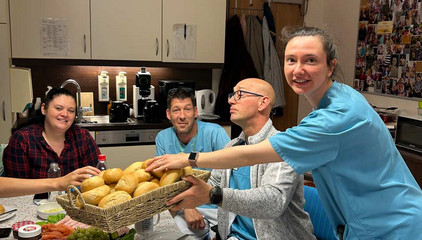 Eine Pflegekraft in blauer Funktionskleidung reicht ihren an einem Frühstückstisch sitzenden Kolleginnen und Kollegen einen Korb mit Brötchen am Internationalen Tag der Pflegenden im Immanuel Haus am Kalksee in Rüdersdorf bei Berlin.