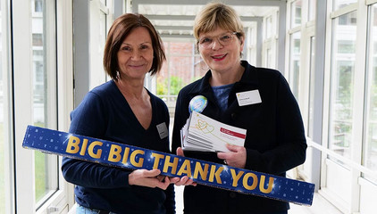 Sabine Kalkhoff, Gesamtleiterin Residenz am Wiesenkamp und Gesellschaft für Diakonie, steht mit einer Mitarbeiterin in einem Durchgang und hält Gutscheine und eine Schild mit der Aufschrift "Big Big Thank You" in die Kamera am Internationalen Tag der Pflegenden in Hamburg-Volksdorf.