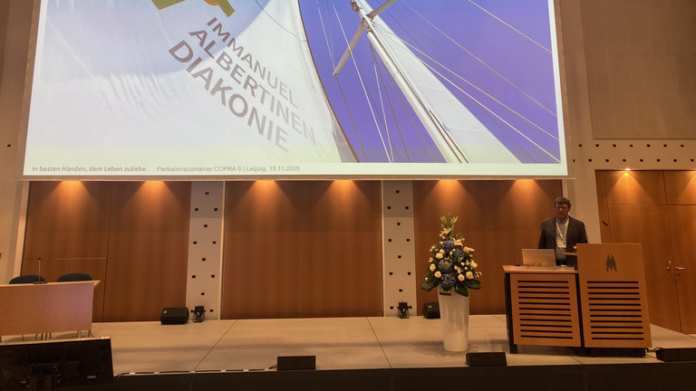 Der Leiter der Perfusiologie am Immanuel Klinikum Bernau Herzzentrum Brandenburg Torsten Müller stellt den Perfusionscontainer am Rednerpult auf der Bühne mit einer Leinwand bei der Internationalen Jahrestagung der Deutschen Gesellschaft für Perfusionsmedizin und der Fokustagung Herz der Deutschen Gesellschaft für Thorax-, Herz- und Gefäßchirurgie in Leipzig vor Der Leiter der Perfusiologie am Immanuel Klinikum Bernau Herzzentrum Brandenburg Torsten Müller stellt den Perfusionscontainer am Rednerpult auf der Bühne mit einer Leinwand bei der Internationalen Jahrestagung der Deutschen Gesellschaft für Perfusionsmedizin und der Fokustagung Herz der Deutschen Gesellschaft für Thorax-, Herz- und Gefäßchirurgie in Leipzig vor