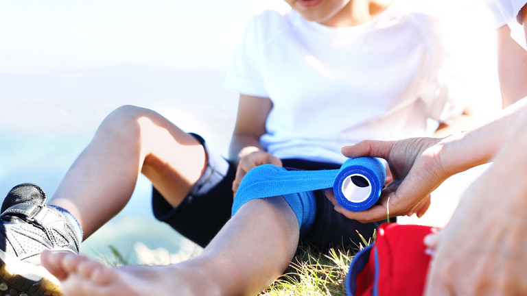 Ein Kinderbein wird mit einem vlauen Verband verarztet