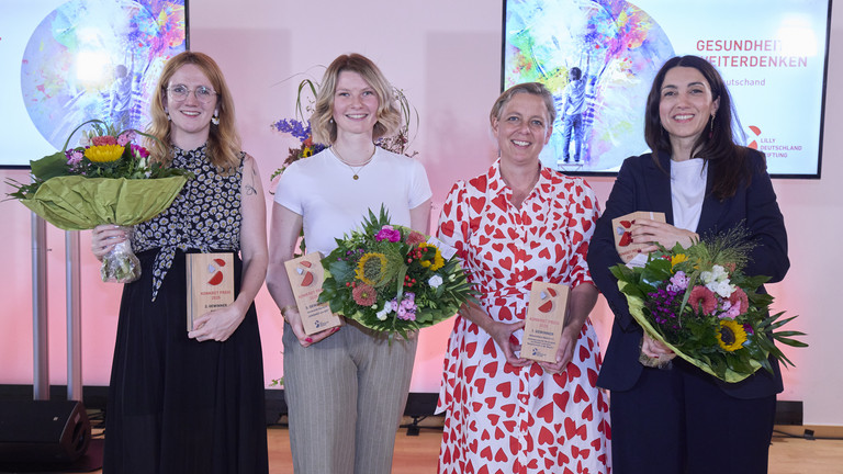 Die Gewinnerinnen stehen auf der Bühne nebeneinander mit Blumensträußen