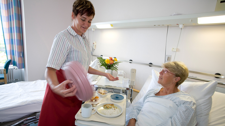 Servicekraft bringt Essen an Patientenbett - Pflege - Immanuel Klinikum Bernau