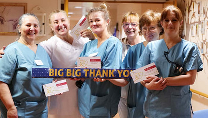 Sechs Pflegekräfte in Funktionskleidung stehen lachend nebeneinander und halten ein Querschild mit der Aufschrift "Big Big Thank You" und Geschenkkarten in die Kamera am Internationalen Tag der Pflegenden in Hamburg-Volksdorf.