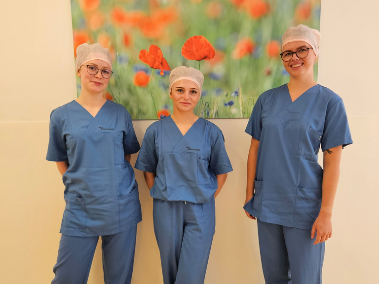 Auszubildende zur OTA und ATA im Immanuel Klinikum Bernau stehen nebeneinander vor einer Wand mit einem Bild