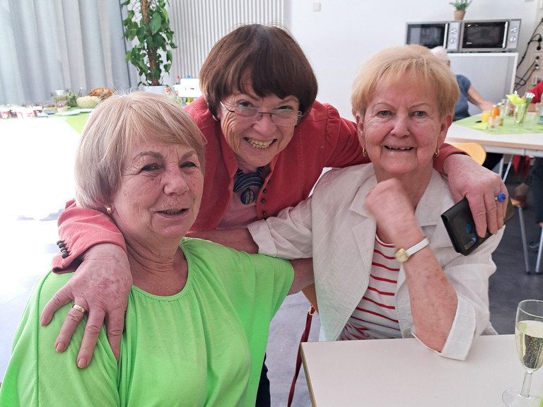 Drei ehemalige Kolleginnen beim Ehemaligentreffen des Immanuel Klinikum Bernau Arm in Arm an einem Tisch